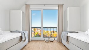 A hotel room with two beds, a balcony with a view of the sea, and a wooden floor. - Baltic Sea vacation apartment "Meeresfl üstern" with sea view, sauna and close to the beach (Olpenitz)