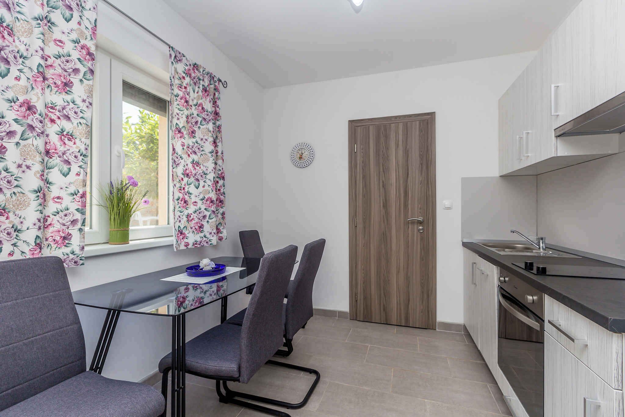 A compact kitchen with a dining area, a wooden door, and a window with floral curtains.