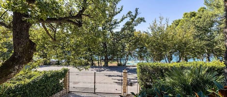 A paved pathway leading to a gated entrance, surrounded by lush greenery and trees.