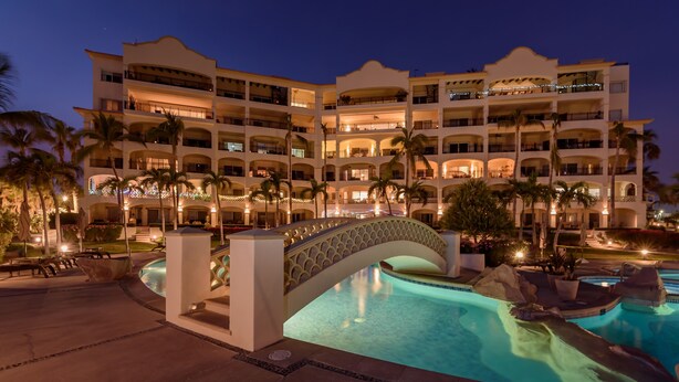 Un hotel de varios pisos con piscina, palmeras y un puente.