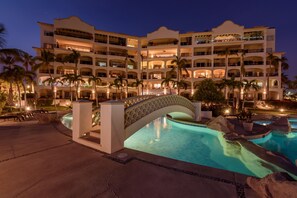 A multi-story hotel with a swimming pool, palm trees, and a bridge. - Cozy 2-Bedroom Condo in Beautiful San José del Cabo, just steps to the Beach!  (San José del Cabo)