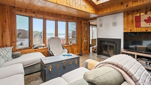 A cozy cabin interior with wooden walls, a fireplace, a television, and a large window overlooking a scenic view.