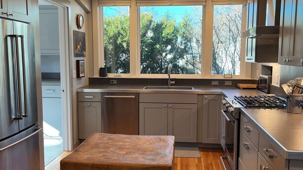 A modern kitchen with a large island, stainless steel appliances, and a view of trees through the windows. - The Perfect In Town Home Away from Home (Durango)