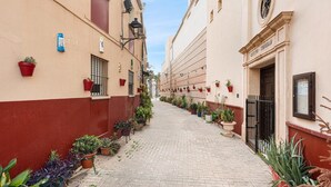 A narrow cobblestone alley lined with potted plants and buildings with red and beige facades.