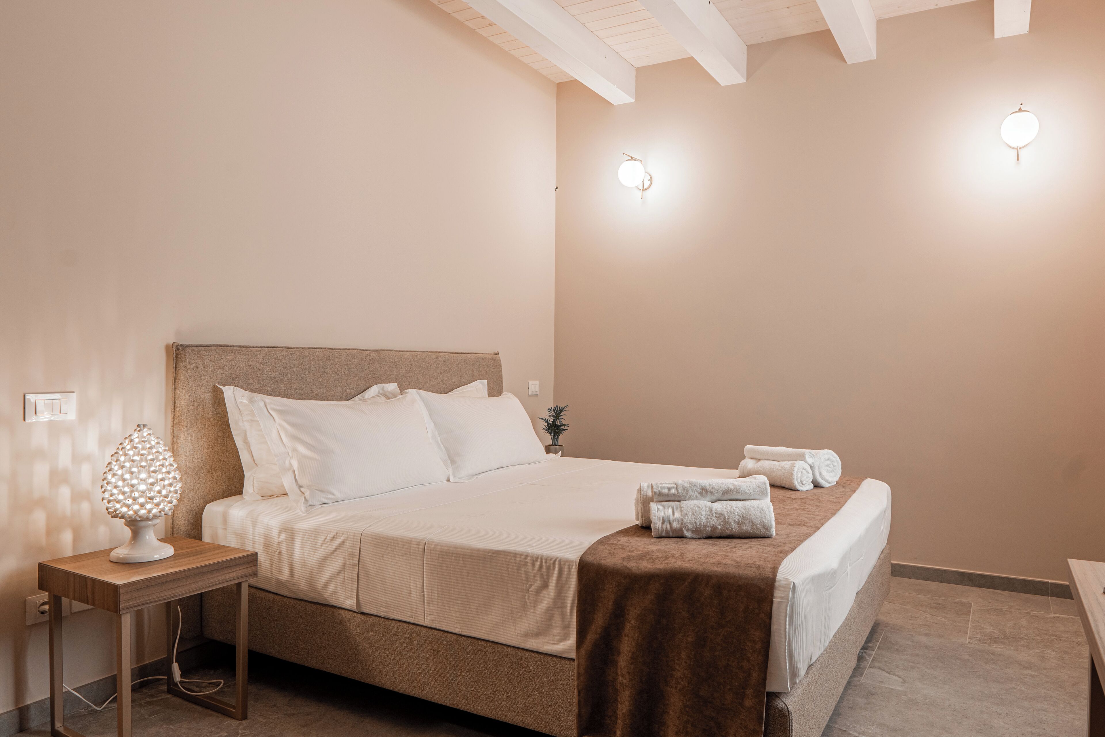 A neatly made bed with white linens, a brown headboard, and a bedside table with a lamp.
