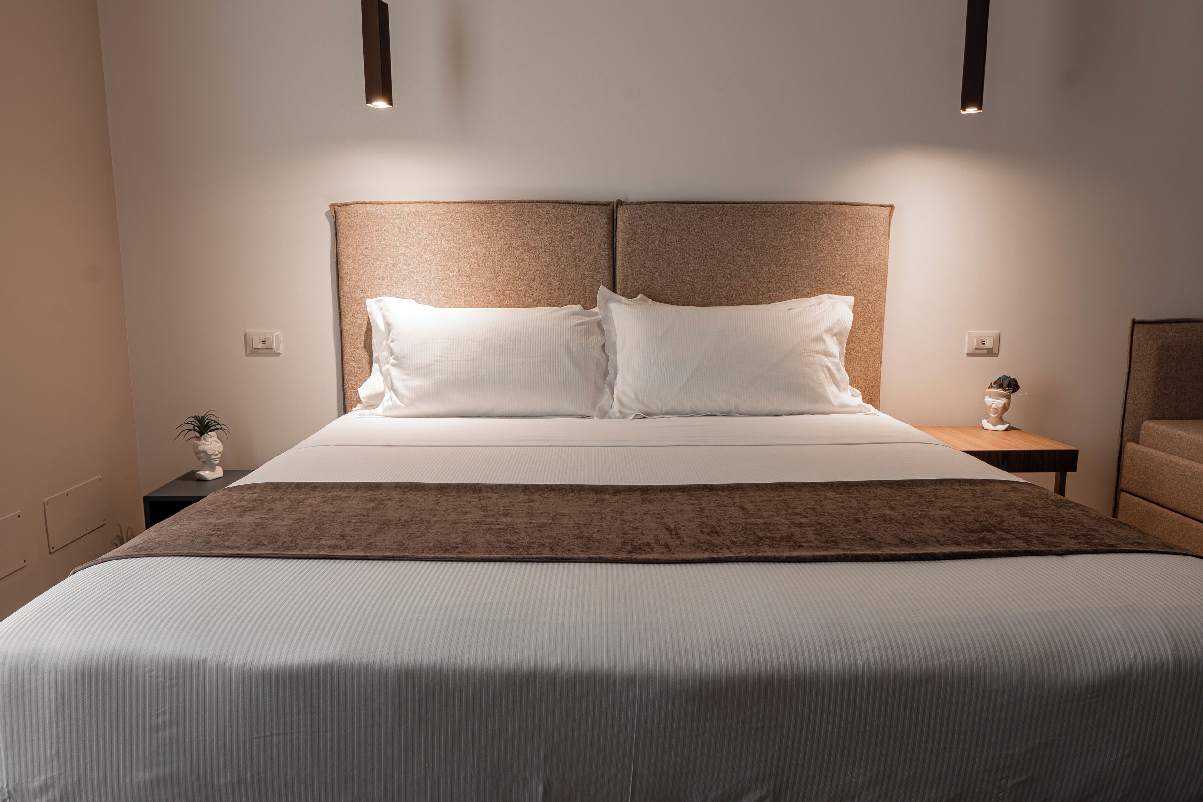 Un lit bien fait, avec une tête de lit marron, du linge de lit blanc et deux tables de chevet ornées de petits objets décoratifs.