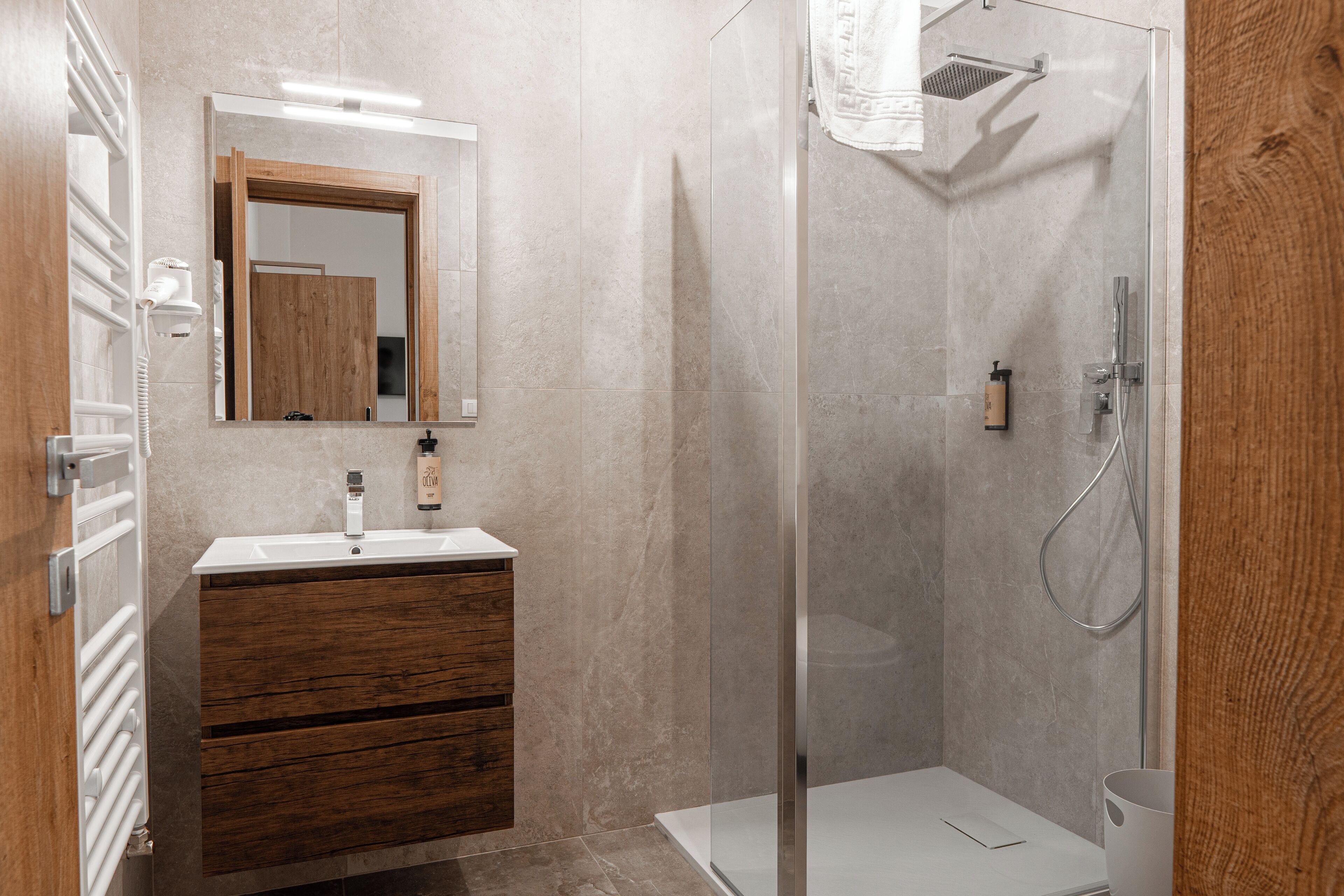 A modern bathroom with a wooden vanity, a glass shower enclosure, and a white sink.