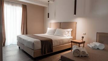 Une chambre d’hôtel moderne avec un grand lit, une table de chevet avec des serviettes et une petite table sur laquelle est posé un vase.