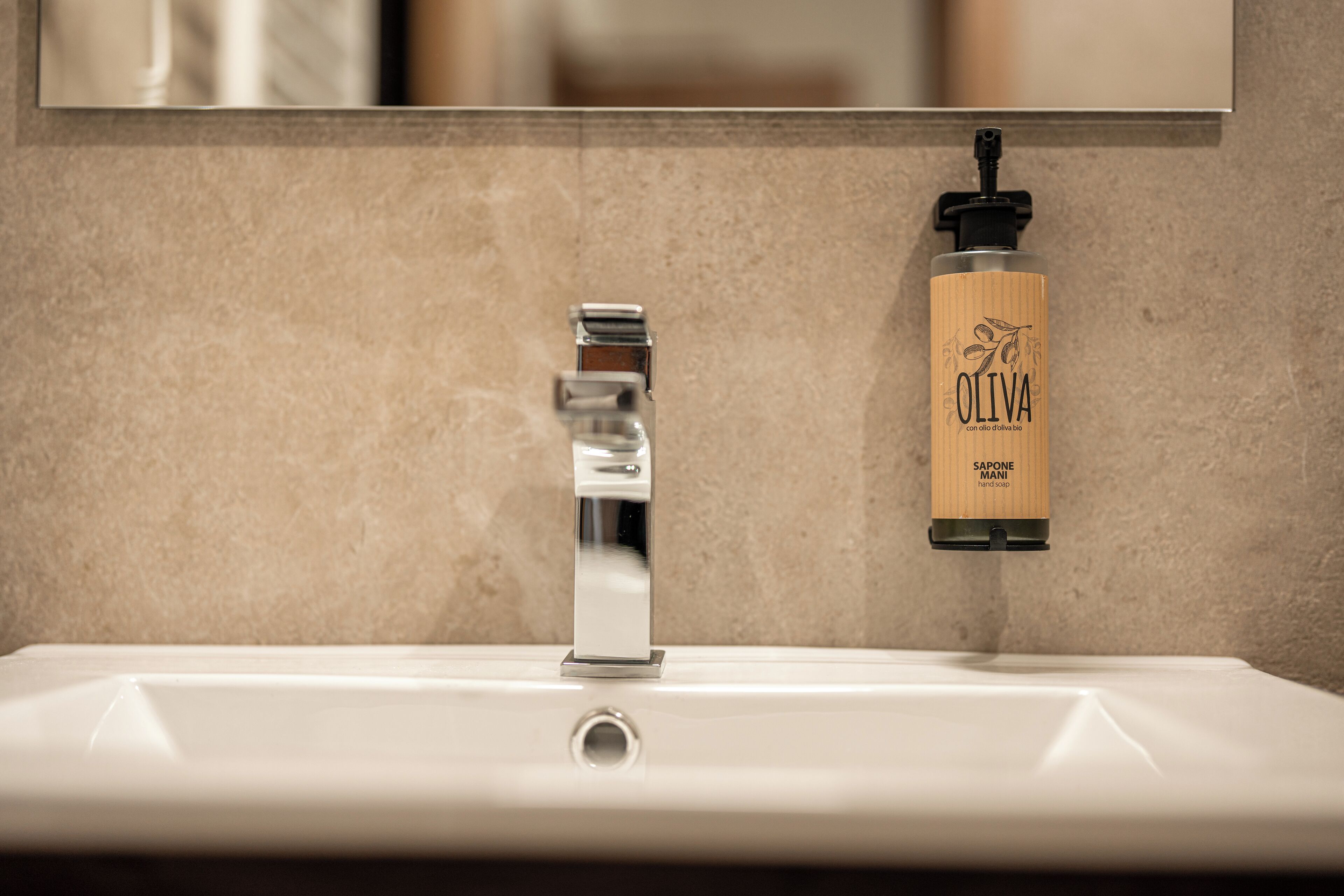 A bathroom sink with a chrome faucet and a bottle of olive oil soap.