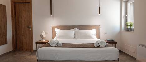 A modern bedroom with a large bed, wooden headboard, bedside tables, and a window with a view.