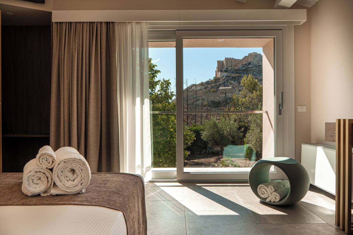 A hotel room with a bed, a view of a mountain, and a balcony with a chair.