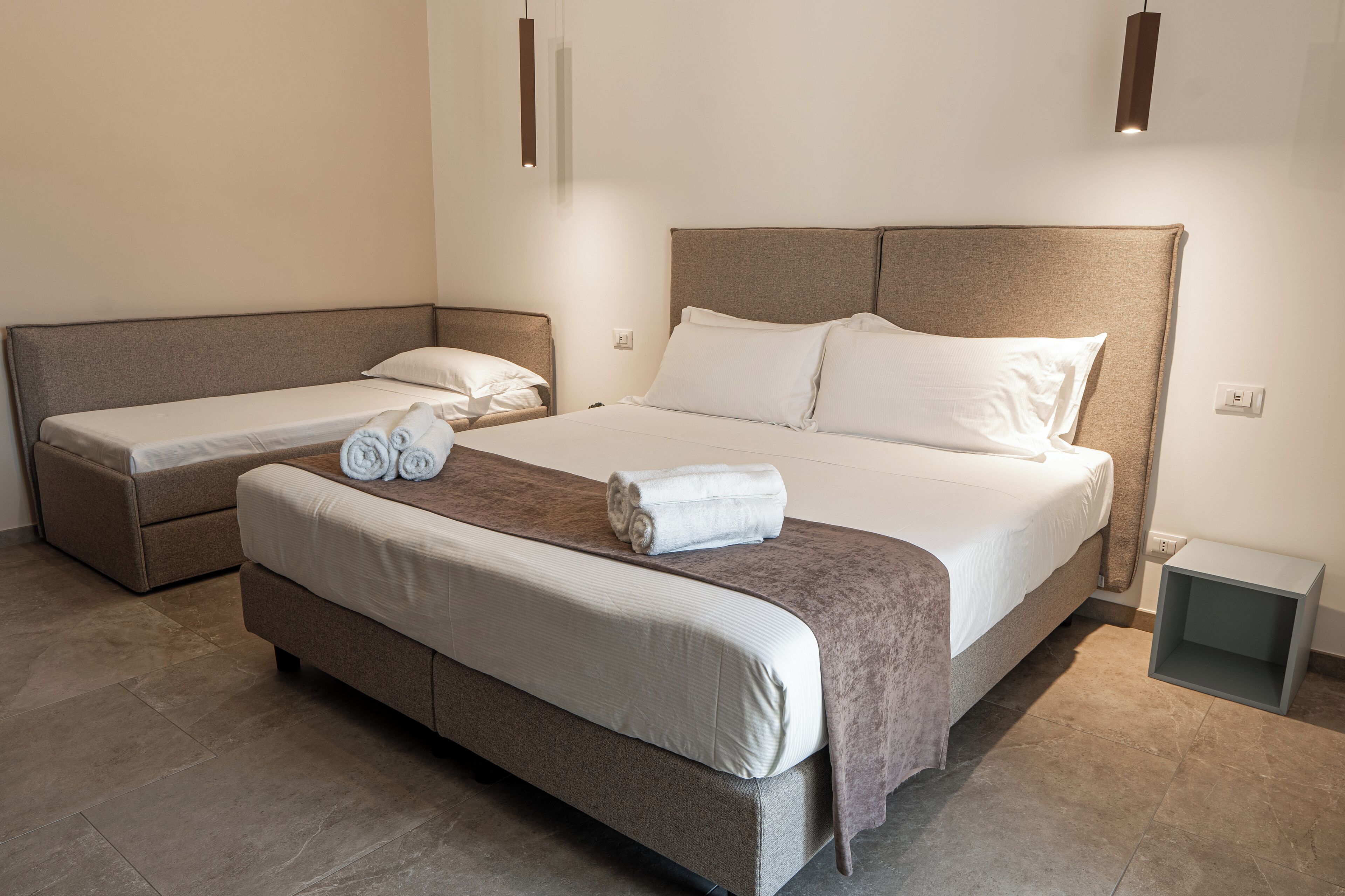 Un dormitorio con una cama grande, una cama más pequeña y un sofá. Hay toallas sobre las camas.