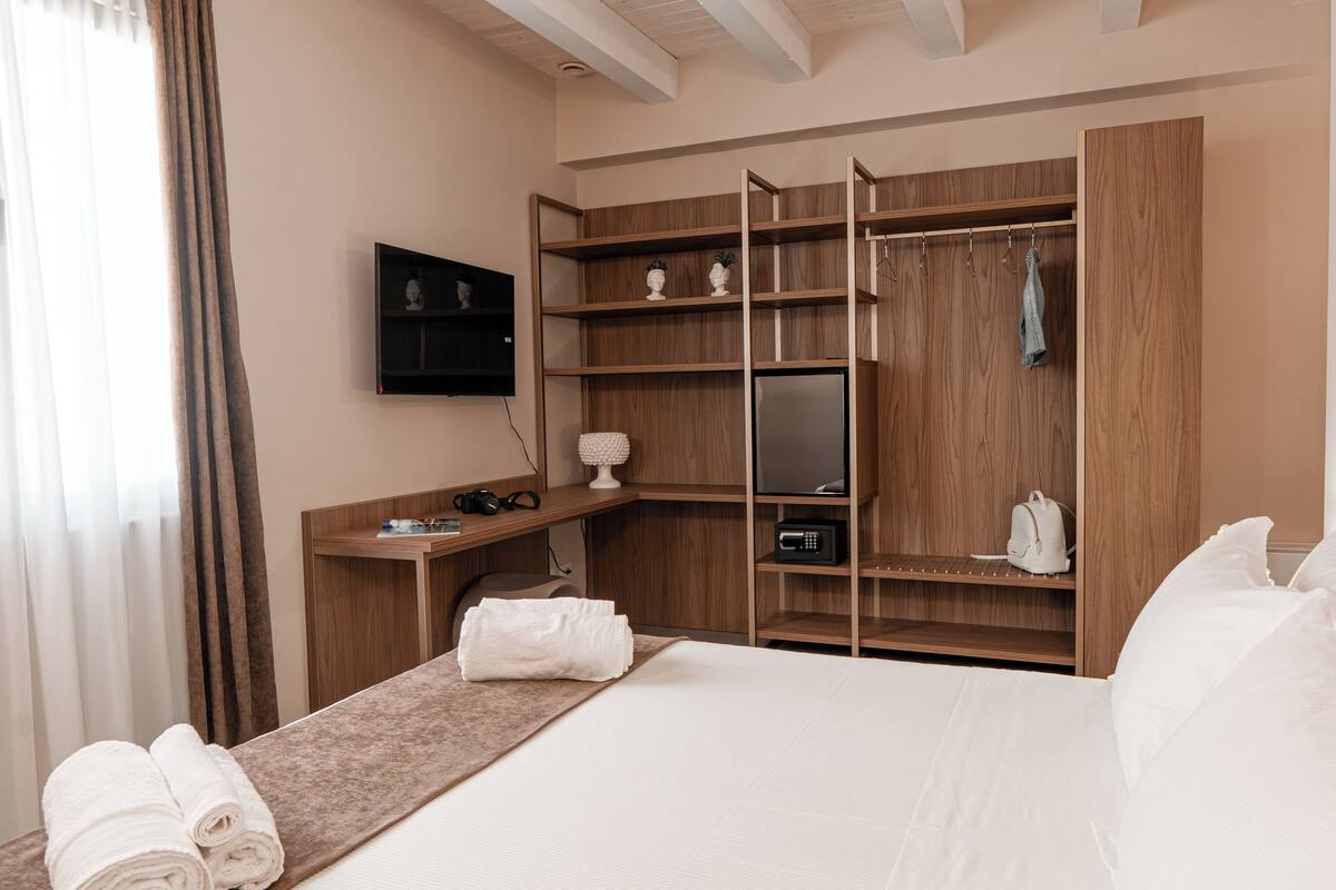 A hotel room with a bed, a wooden wardrobe, a TV, and a desk with a lamp.