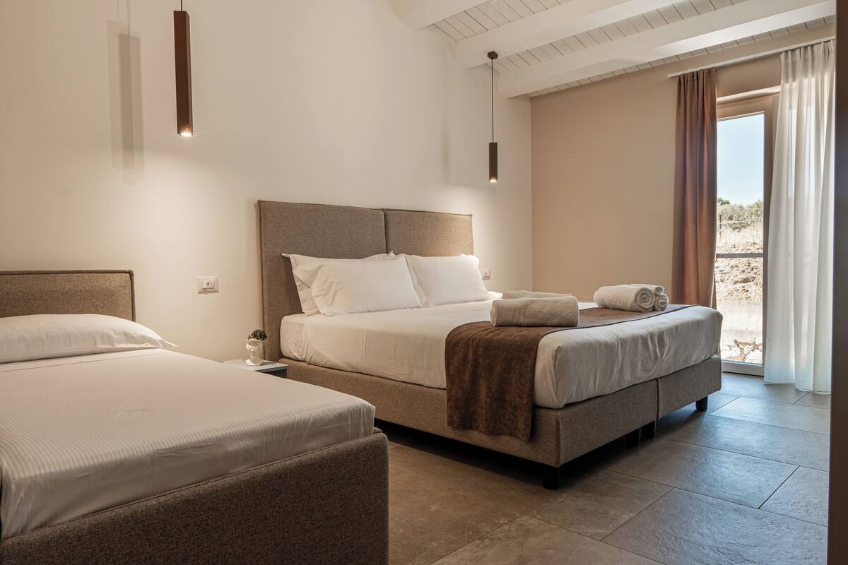 A modern hotel room with a large bed, a smaller bed, and a sofa.