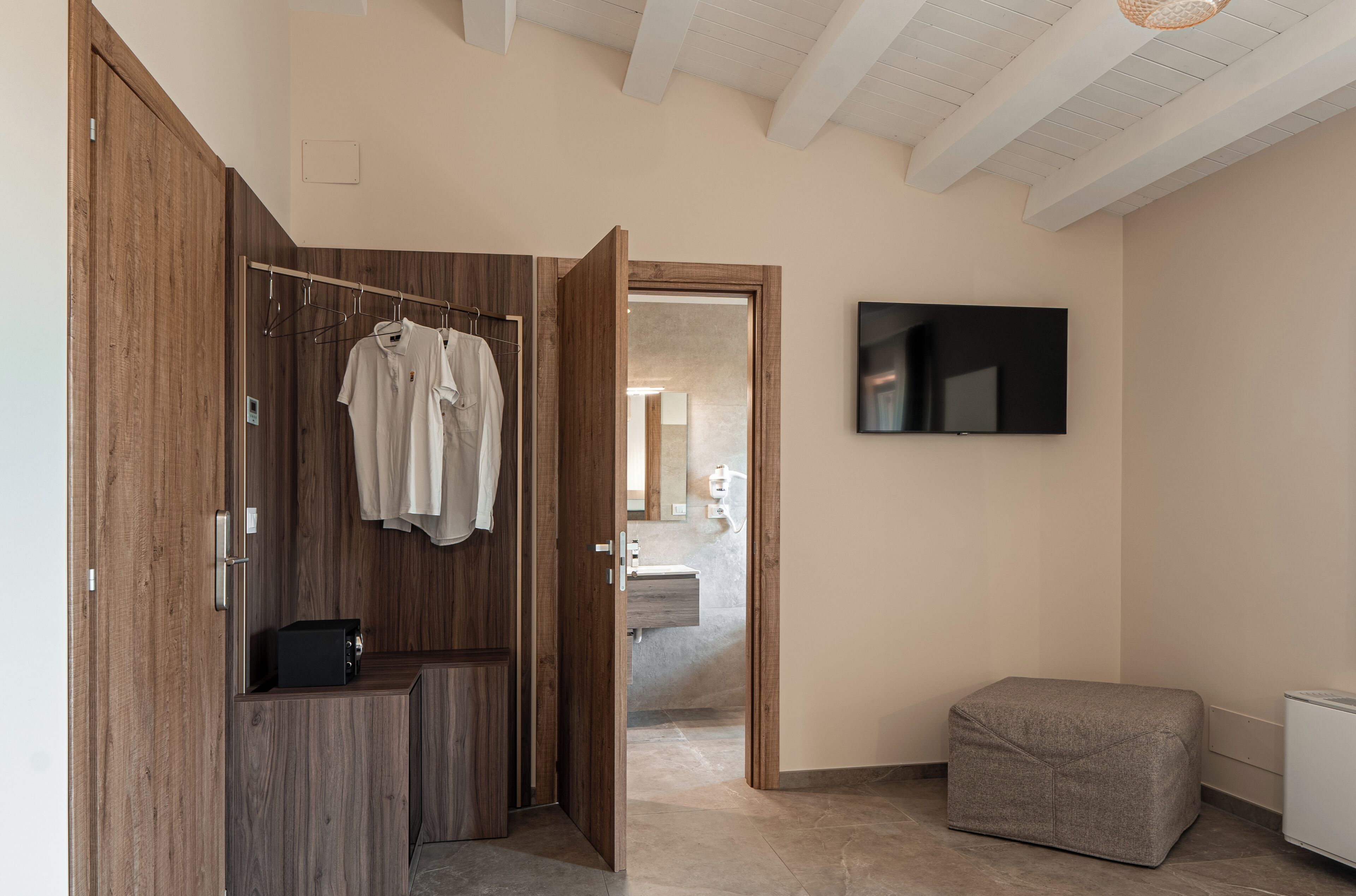 A modern bathroom with a wooden wardrobe, a hanging shower curtain, and a flat-screen TV mounted on the wall.