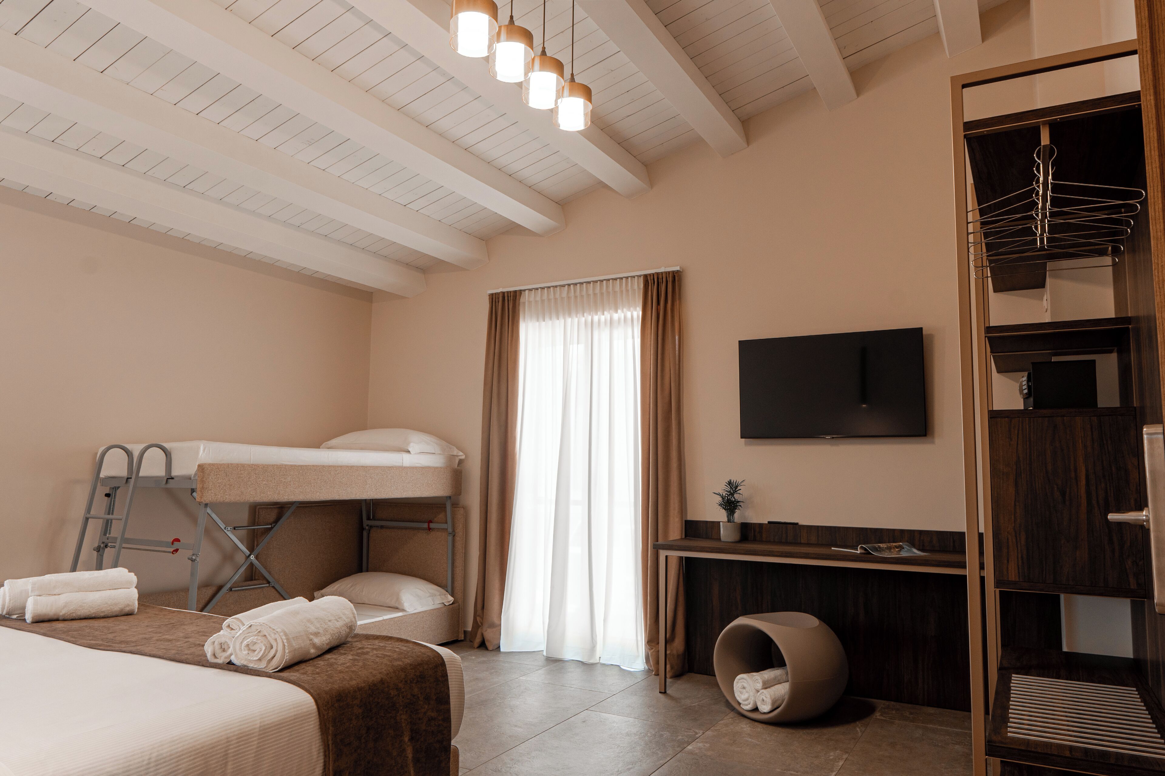 A modern hotel room with a bunk bed, a desk, a TV, and a wardrobe.