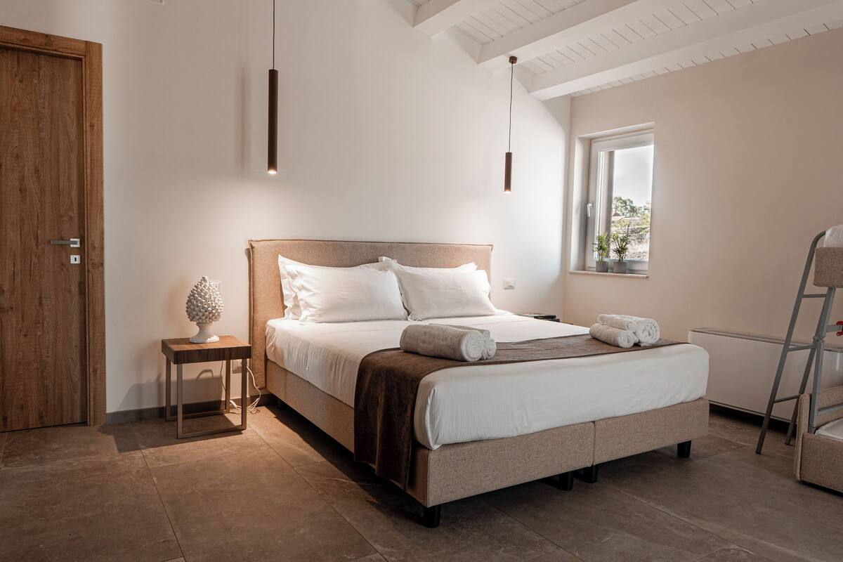 A bedroom with a bed, bedside table, lamp, window, and a wooden door.