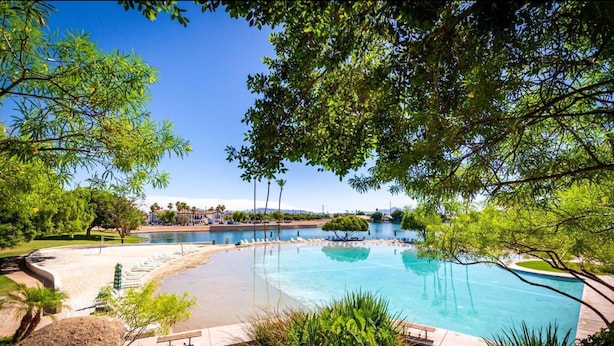 Une grande piscine extérieure entourée d’une végétation luxuriante, sous un ciel bleu et dégagé.