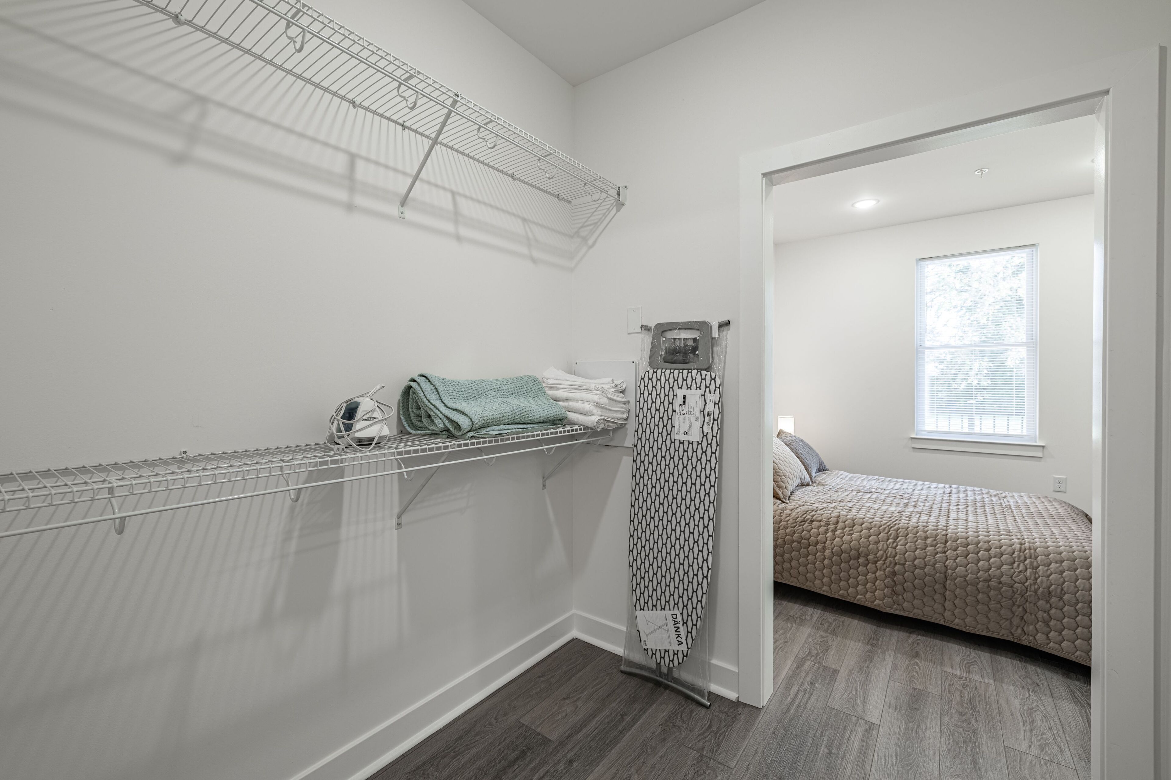 A bedroom with a bed, a window, and a walk-in closet with shelves and a drying rack.
