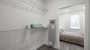 A bedroom with a bed, a window, and a walk-in closet with shelves and a drying rack.