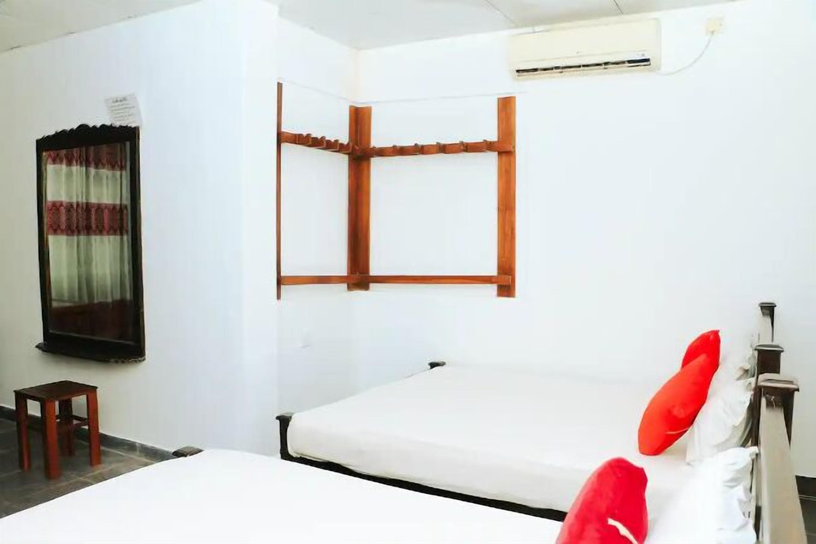 A single bed with a wooden headboard, a small wooden stool, and a window with curtains.