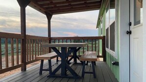 Une terrasse en bois avec une table et des bancs, un espace abrité et une vue sur le paysage.