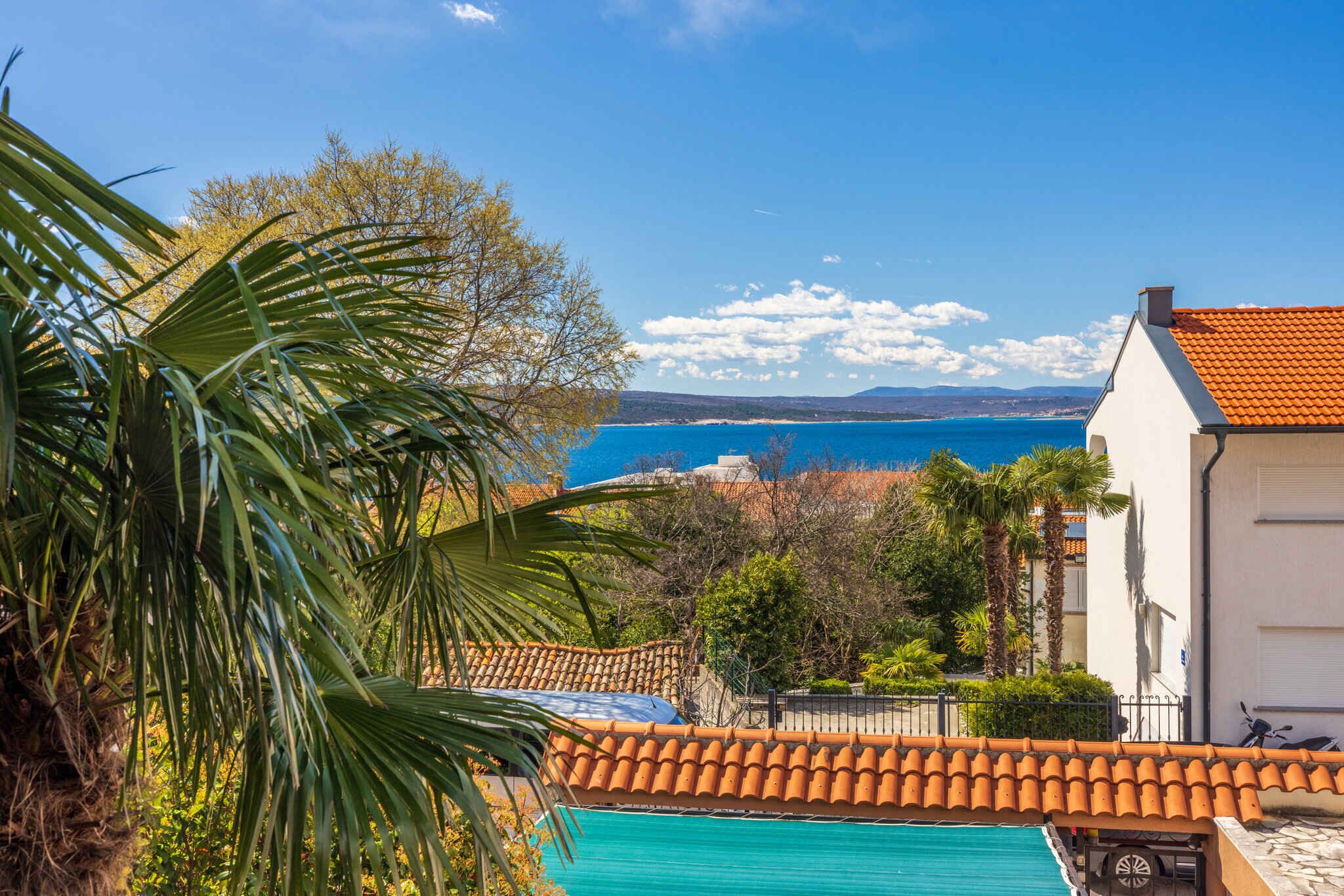 A coastal view with a swimming pool, palm trees, and a building with a tiled roof.