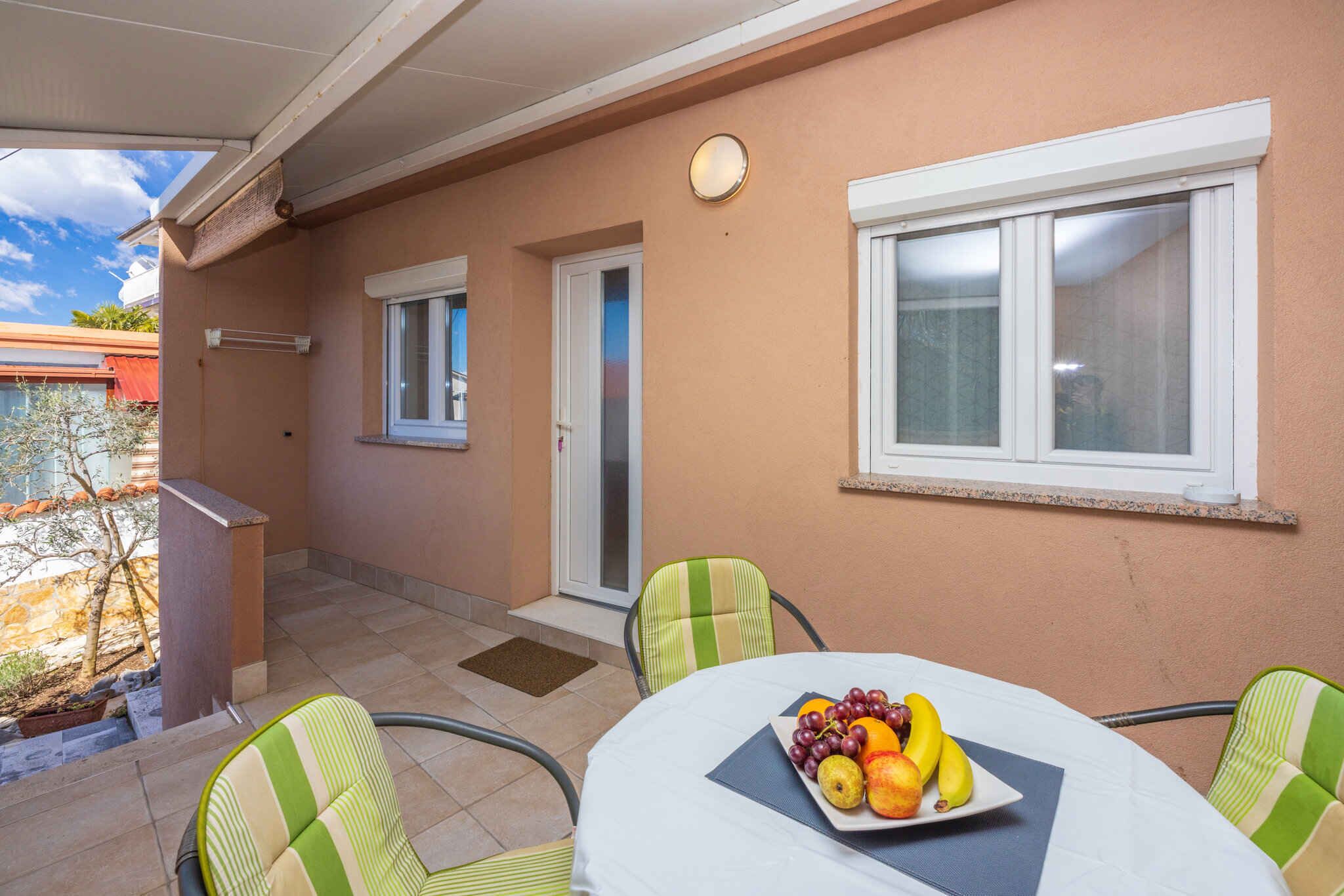 Uma área de estar coberta ao ar livre, com uma mesa posta para dois, e um prato de frutas.