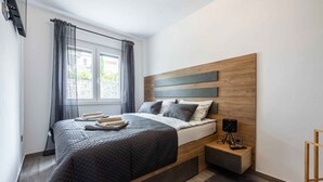 Un dormitorio moderno con una cama grande, una mesita de noche con lámpara y vistas al exterior a través de una ventana con cortinas.