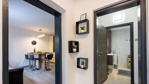 Un interior moderno con área de cocina, taburetes de bar y una mesa de comedor. Se observan estanterías de marco negro con plantas en macetas.
