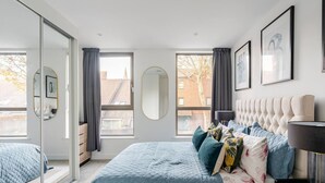 Ein modernes Schlafzimmer mit einem großen Bett, einem Spiegel und Blick auf die Stadt.