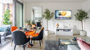 Ein modernes Wohnzimmer mit Essbereich, großen Fenstern und einem Flachbildfernseher an der Wand.