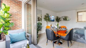 Ein moderner Essbereich mit einem Glastisch, orangefarbenen Stühlen und einem grauen Sofa.