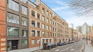Eine Reihe moderner Backsteinbauten mit großen Fenstern und Balkonen, ein klarer Himmel und parkende Autos auf der Straße.