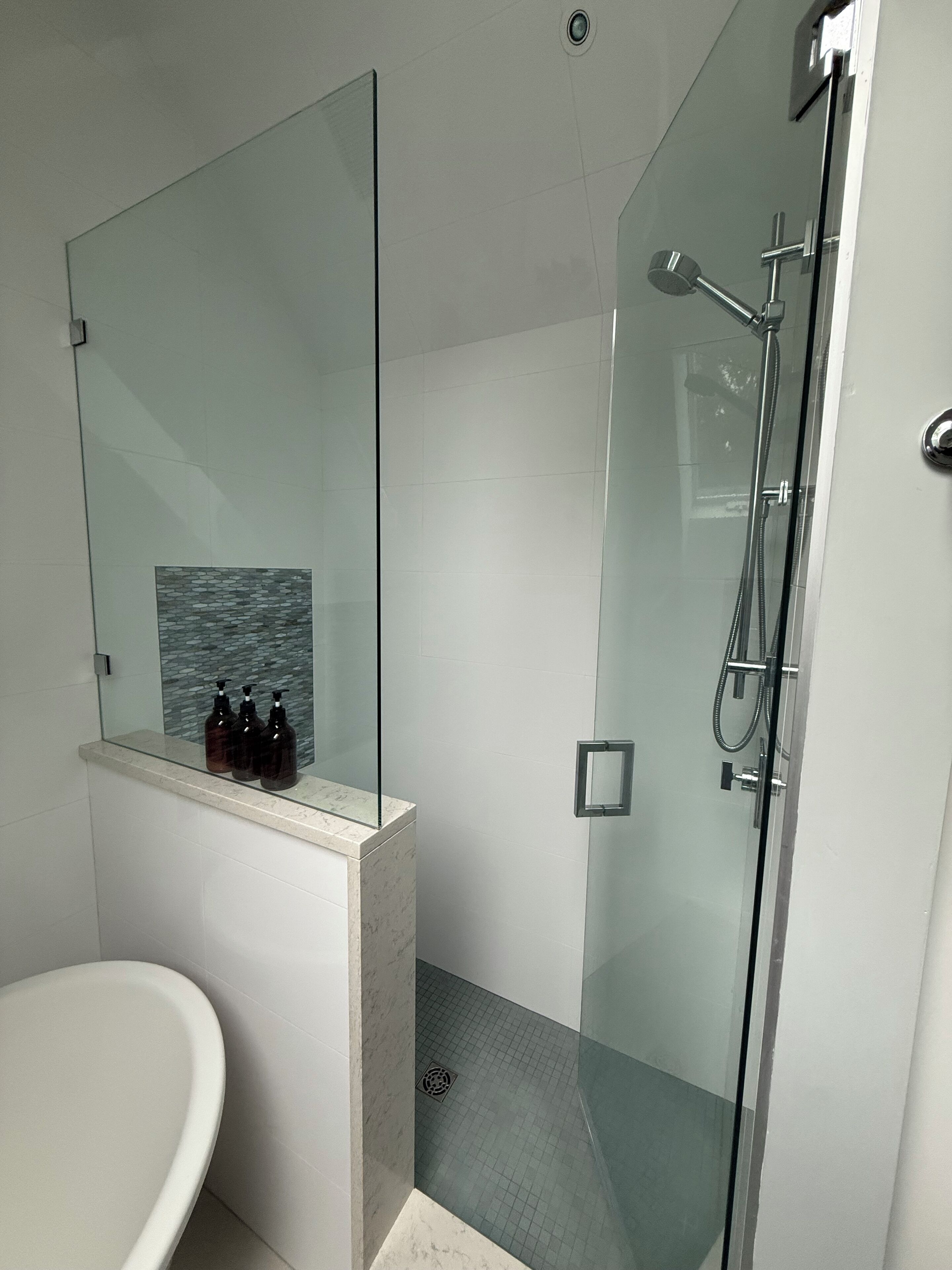 Un baño moderno con cabina de ducha de vidrio, lavamanos de mármol y espejo de vidrio.