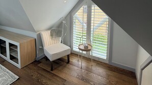 A cozy attic bedroom with a sloped ceiling, a white chair, a small table, and a wooden cabinet.