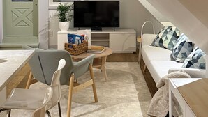 A modern loft bedroom with a sloped ceiling, a flat-screen TV, a sofa, a dining table, and a chair.