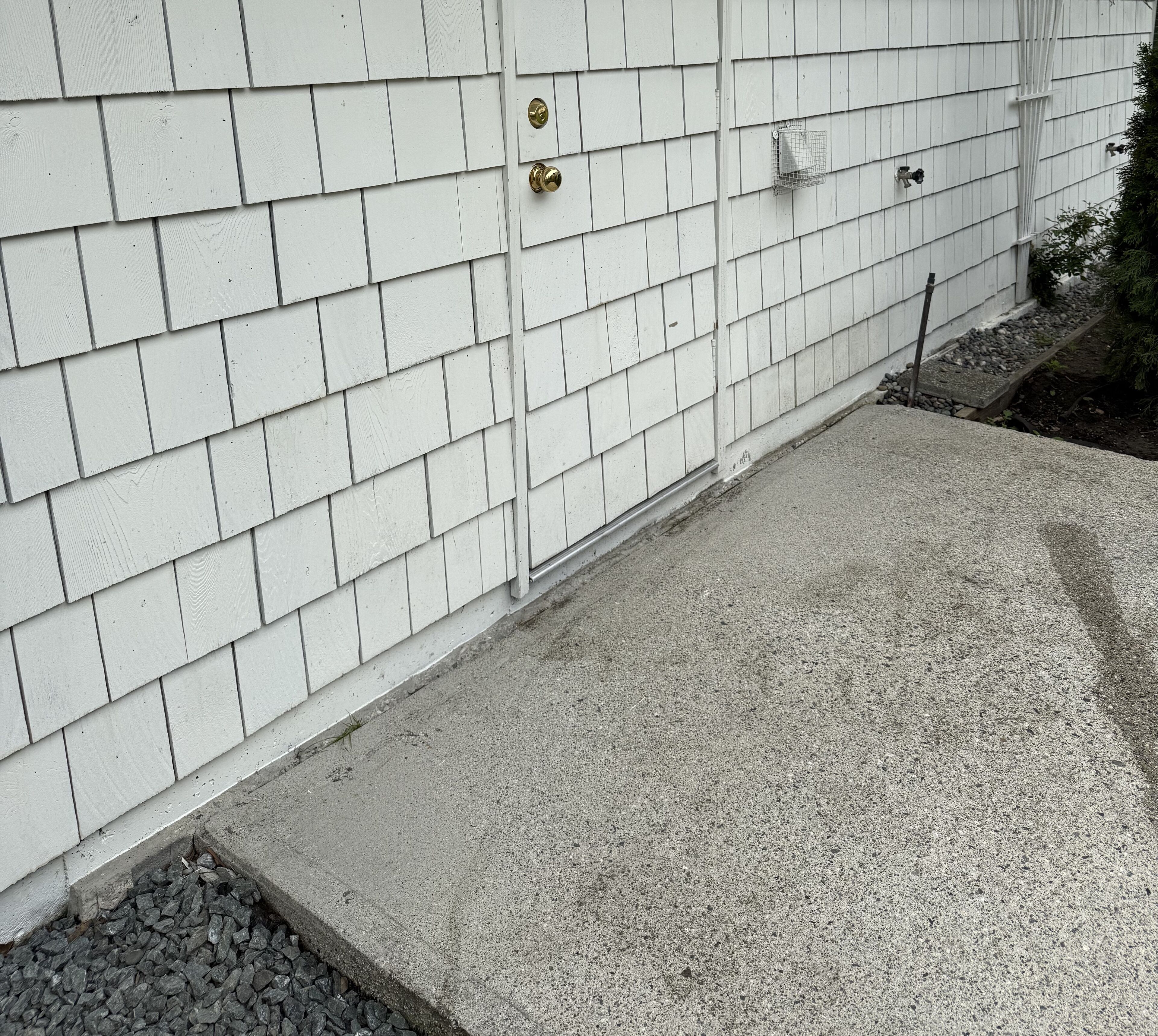 Eine weiße Außenwand mit einer Betonauffahrt und einem kleinen Garten.