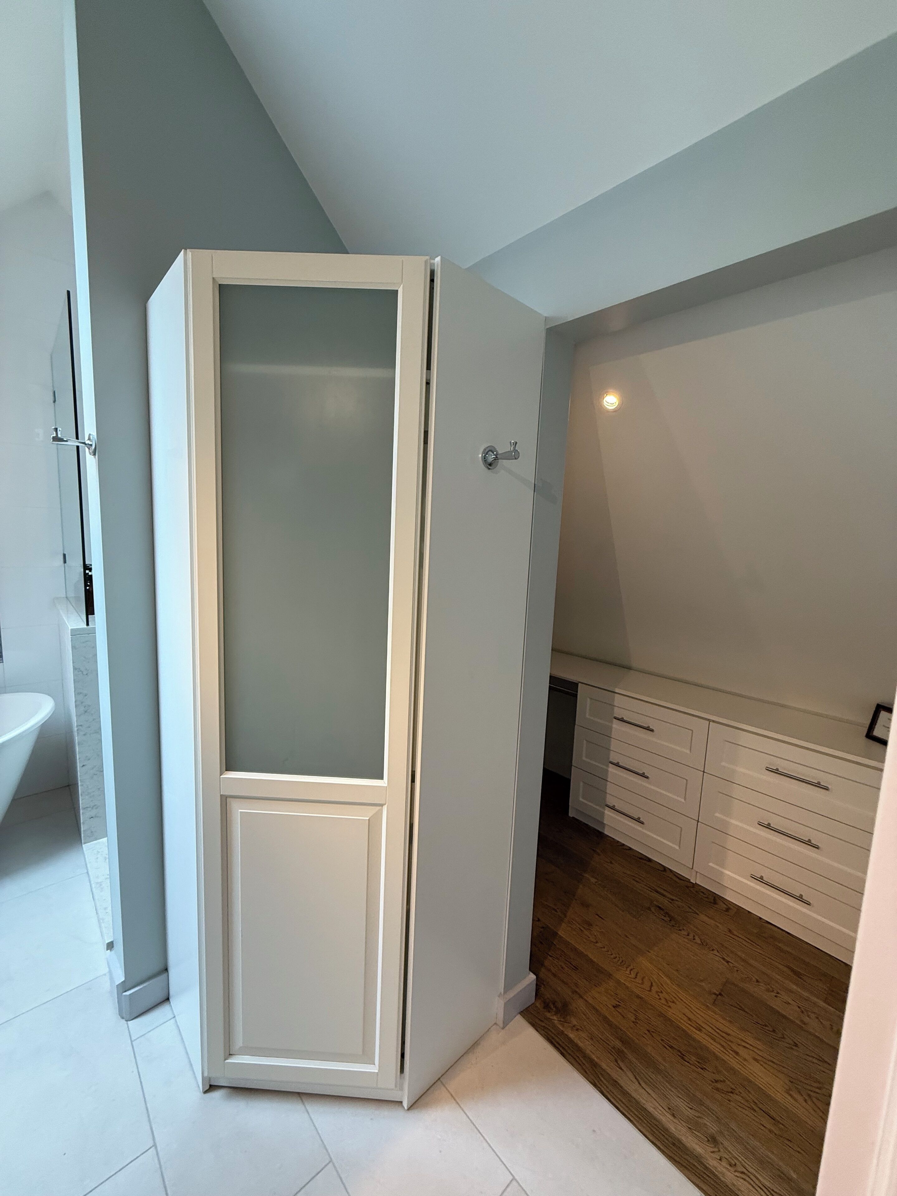Una habitación con un armario blanco, suelo de madera y un lavabo blanco.