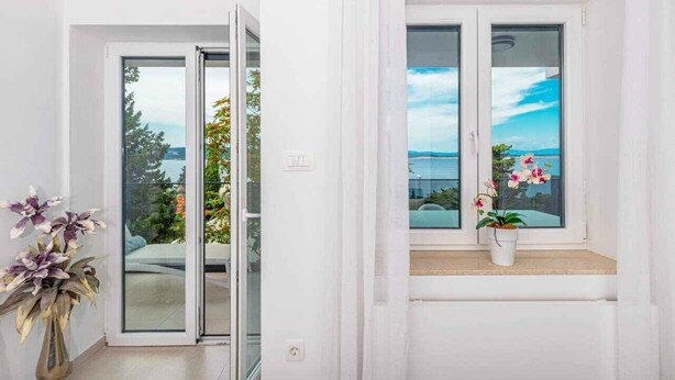 Une pièce dotée d’une porte-fenêtre coulissante donnant sur un balcon avec vue sur un plan d’eau et des arbres. Un pot d’orchidée est posé sur le rebord de la fenêtre.