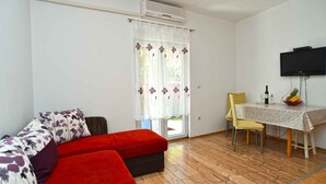 A room with a red sofa, a dining table with chairs, and a television mounted on the wall. - Holiday apartment with air conditioning, pool (Valbandon)