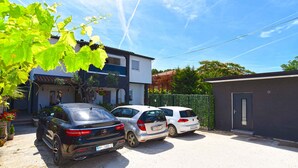 A parking area with three cars parked in front of a two-story house with a balcony. - Holiday apartment with air conditioning, pool (Valbandon)