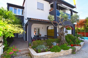A two-story house with a balcony, a garden with various plants and flowers, and a small pool in the background. - Holiday apartment with air conditioning, pool (Valbandon)