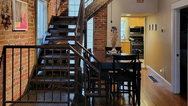 Un loft espacioso con paredes de ladrillo visto, una escalera de madera y una cocina moderna.