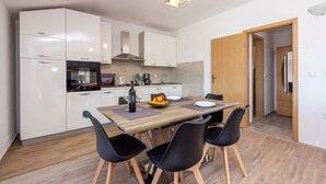 A modern kitchen with white cabinets, a wooden dining table, black chairs, and a fruit bowl.