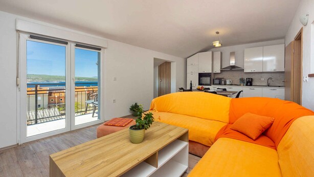 A modern apartment with a balcony, a bright orange sofa, a wooden table, and a kitchen area.