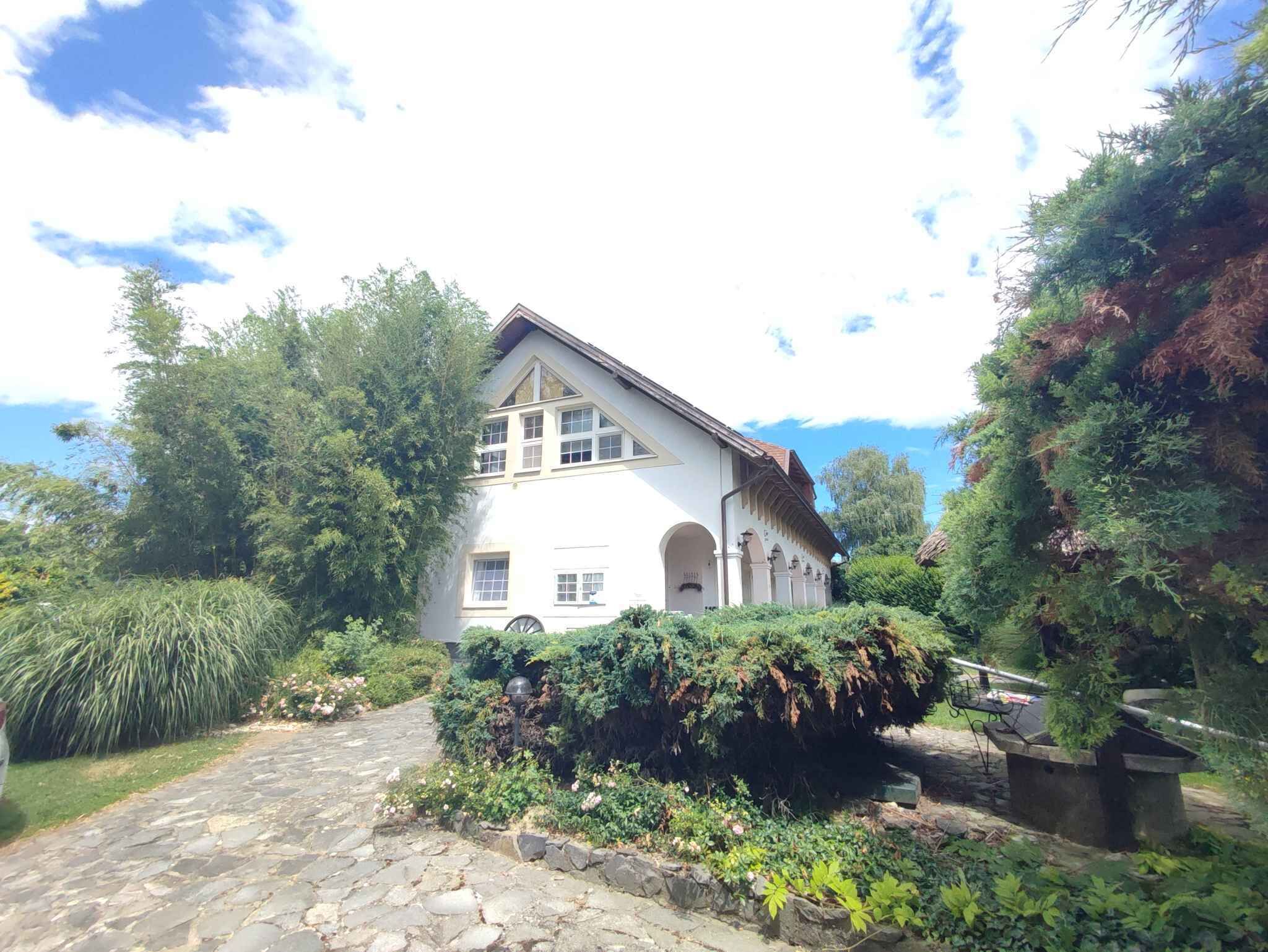 Um edifício branco com um caminho de pedra que o leva até ele, rodeado por vegetação exuberante e árvores.