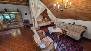 Ein gemütlicher Raum mit einem Bett, einem Sofa und zwei Sesseln. Über dem Sofa hängt eine Chandelieber.