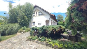 A white building with a stone pathway leading to it, surrounded by lush greenery and trees. - Holiday apartment with wifi and air conditioning (Kehidakustány)