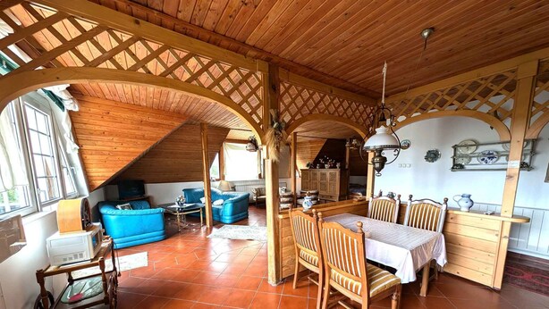 A rustic interior with a wooden ceiling, a dining area with wooden chairs and a table, a blue sofa, and a kitchen area with cabinets and a hanging lamp. - Holiday apartment with wifi and air conditioning (Kehidakustány)